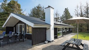 Un área de comedor exterior moderna con mesa y sillas, un espacio de estar cubierto y una chimenea.