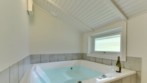 Un baño moderno con una bañera independiente, una ventana y una botella de vino sobre el mostrador.