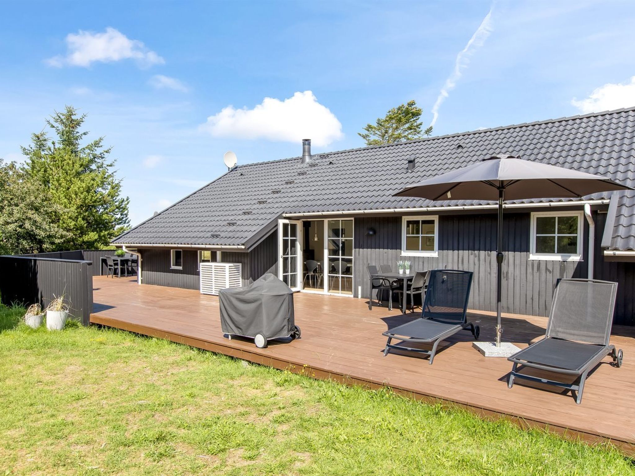 Ein Haus mit überdachter Terrasse, einem Esstisch und Gartenmöbeln.