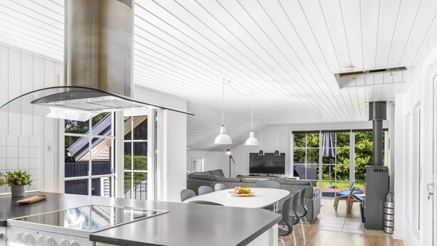 A modern kitchen with a central island, white cabinetry, and stainless steel appliances. There is a dining area with a large window and a view of the outdoors. - "Joseline" - 1.8km from the sea by Interhome (Blåvand)
