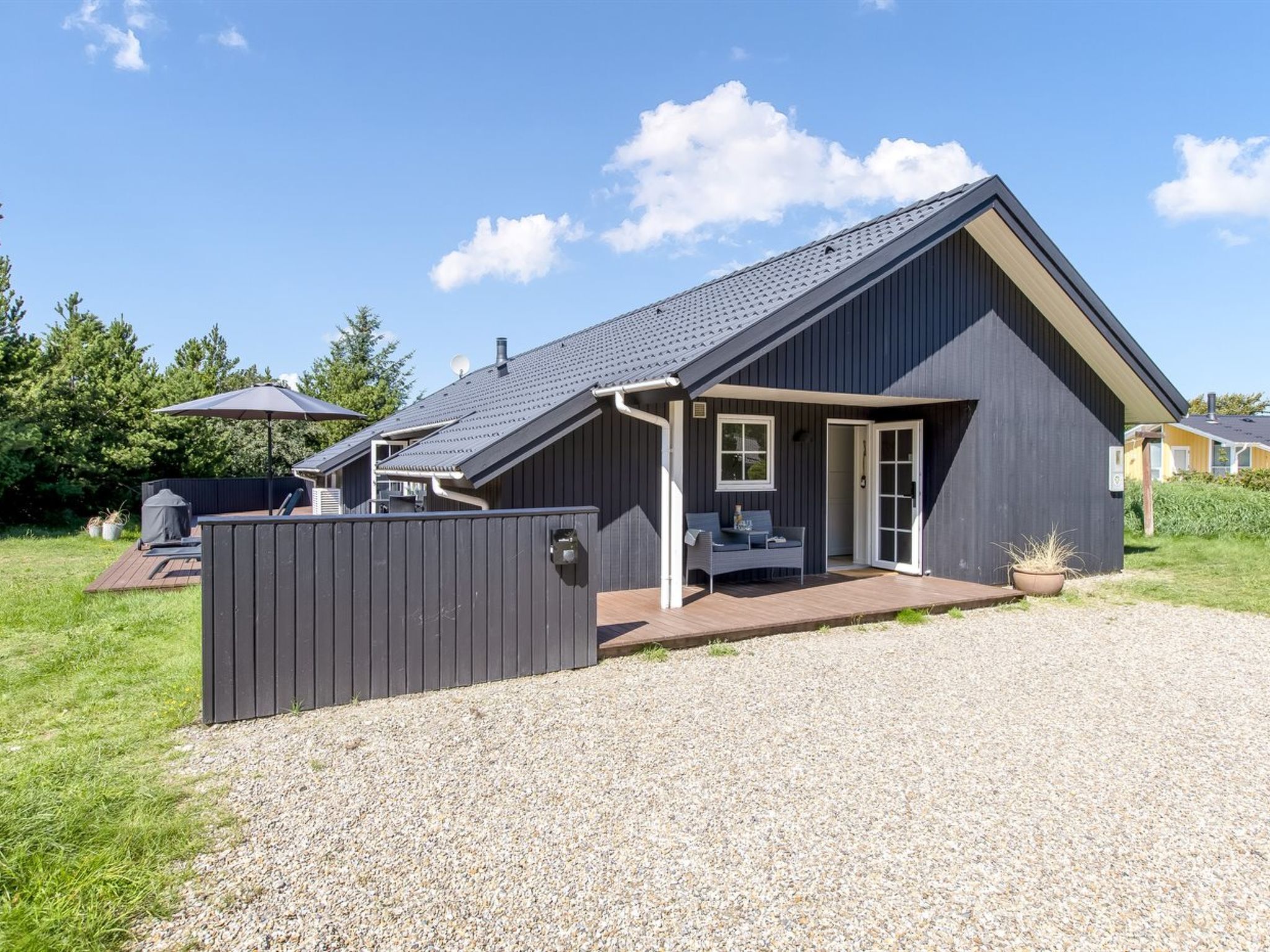 Une maison moderne dotée d’un patio couvert, d’une cour arrière clôturée et d’une allée en gravier.
