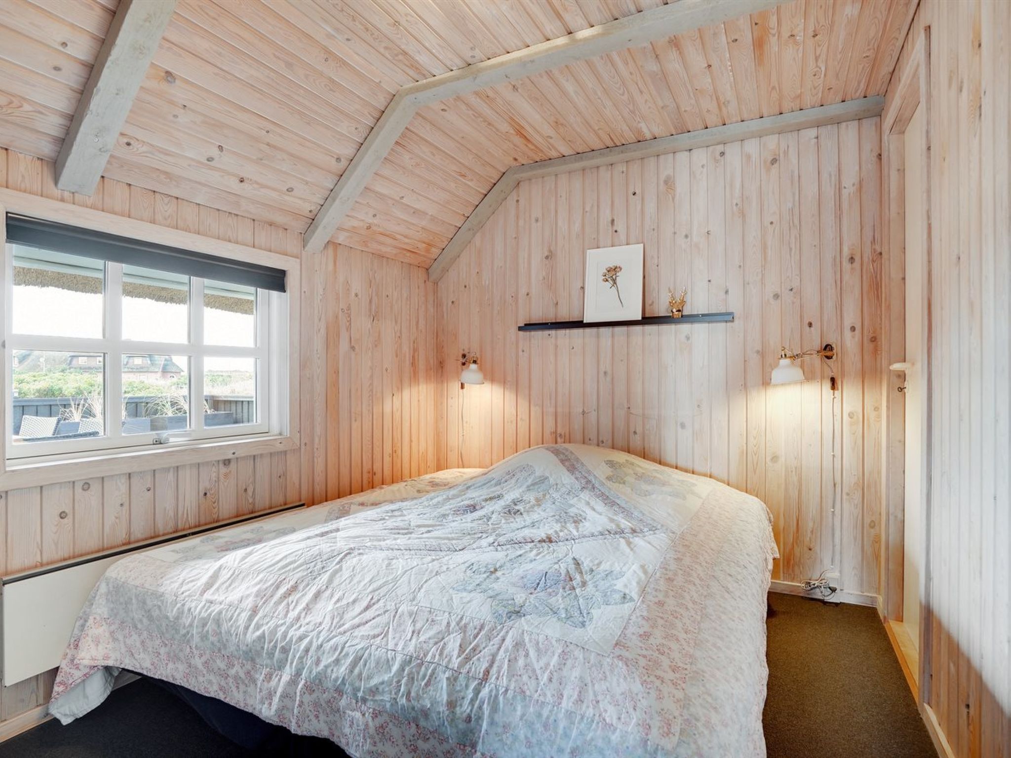 A wooden-paneled room with a bed, a window, and wall-mounted lamps.