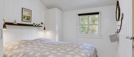 A bedroom with a bed, a window, a wall-mounted coat rack, and a shelf with plants.