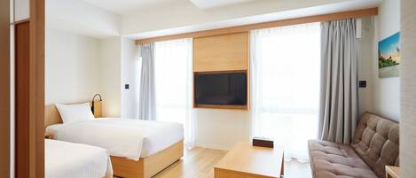 A hotel room with two beds, a sofa, a flat-screen TV, and large windows with curtains.