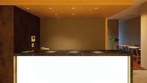 Un espace d’accueil moderne avec un plafond en bois, un comptoir en marbre noir et un coin salon doté de tables et de chaises en bois.