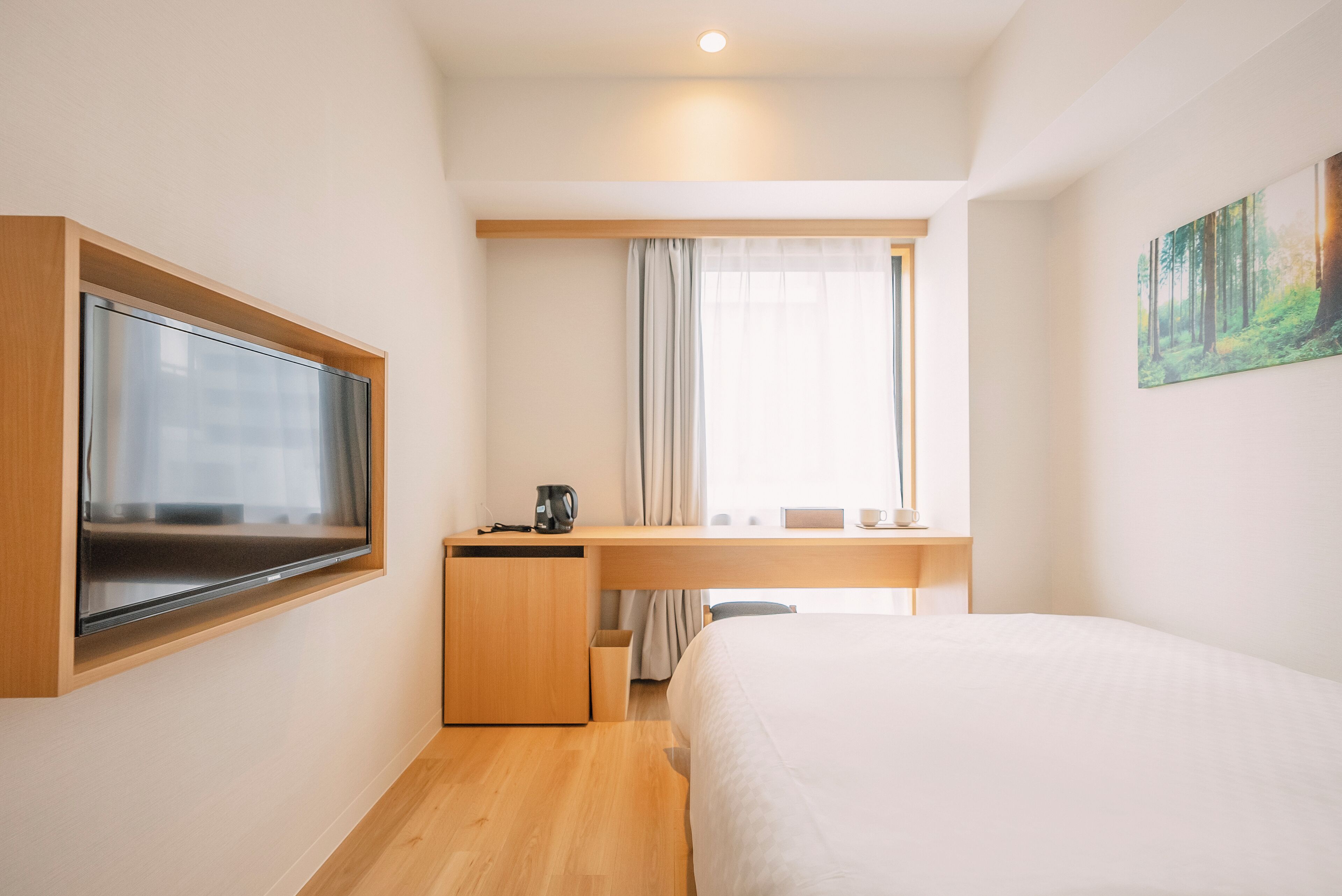 A compact hotel room with a bed, a desk, a television, and a painting on the wall.