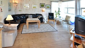 Una sala de estar acogedora con piso de madera, un sofá de cuero negro, una mesa de centro de madera y un televisor sobre un mueble de madera.
