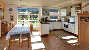Una cocina amplia con piso de madera, un comedor con mesa y sillas, y ventanas grandes que ofrecen vista al exterior.
