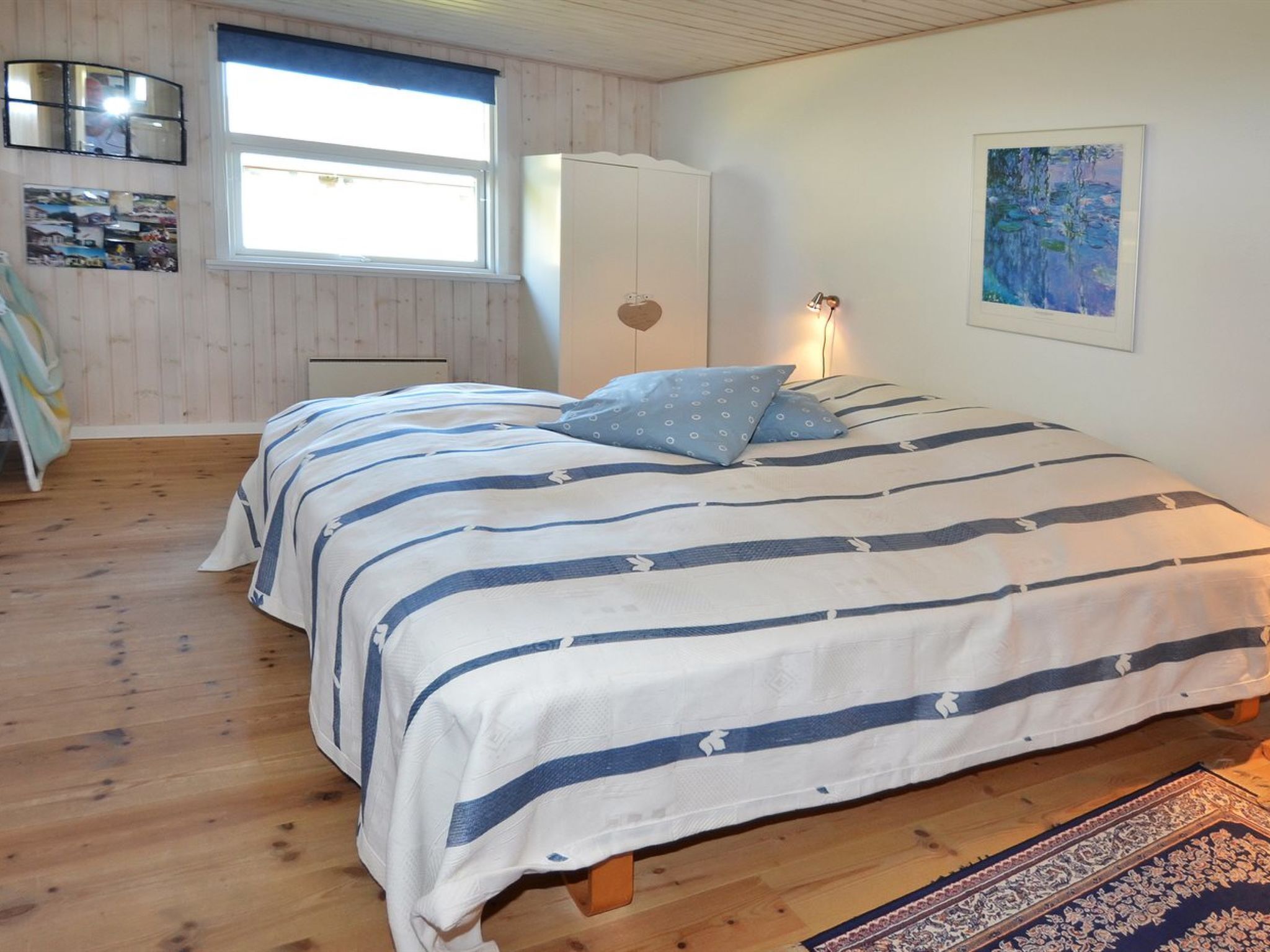 A bedroom with a bed, a window, a wardrobe, and a painting on the wall.