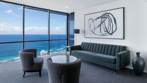 A modern room with a large window, a grey sofa, two armchairs, a round table, and a large abstract painting. - Circle on Cavill Sky Home! (Gold Coast)