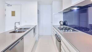 A modern kitchen with stainless steel appliances, a double sink, and a gas stove. - Circle on Cavill Sky Home! (Gold Coast)