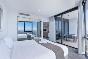 A modern hotel room with a large bed, a seating area with a view, and a balcony with a table and chairs. - Circle on Cavill Sky Home! (Gold Coast)