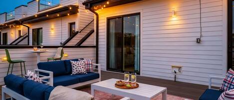 String lights cast a glow across oversized sofas as dusk settles in, the whole rooftop ready for the night ahead