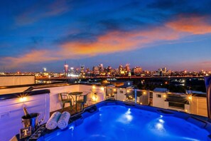Une terrasse sur le toit avec un jacuzzi, des sièges et une vue sur les toits de la ville au crépuscule.