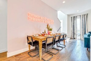 Un espace repas avec une longue table en bois, six chaises et un panneau lumineux au néon accroché au mur.