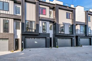 A modern multi-story residential building with grey and black exterior walls, large windows, and garage doors.
