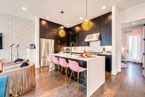 A modern kitchen with dark cabinets, a central island with pink bar stools, and pendant lighting.