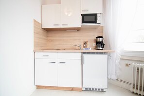 A compact kitchen with white cabinets, a microwave, a coffee maker, and a dishwasher.