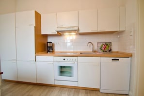 A modern kitchen with white cabinetry, a built-in oven, a dishwasher, and a coffee maker.