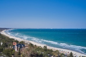 A coastal beach with a clear view of the ocean, a sandy shoreline, and a building with a red roof.