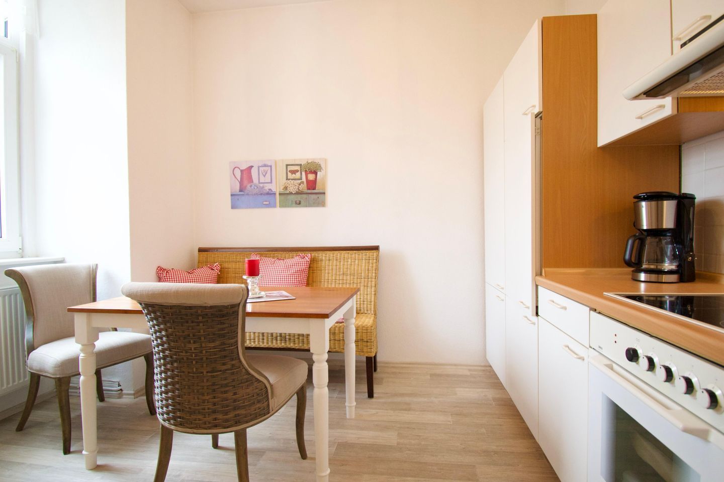 Una cocina pequeña y acogedora con comedor, una silla de mimbre, una mesa de madera y un banco con cojines.