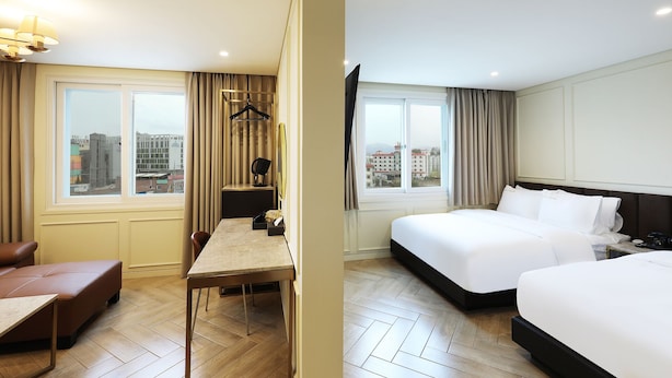 Une chambre d’hôtel équipée d’un lit, d’un bureau, d’une chaise et offrant une vue sur la ville grâce à de grandes fenêtres.