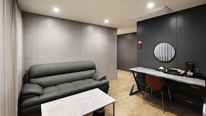 Une pièce moderne et minimaliste, avec un canapé gris, une petite table, un miroir rond et un bureau avec une chaise.