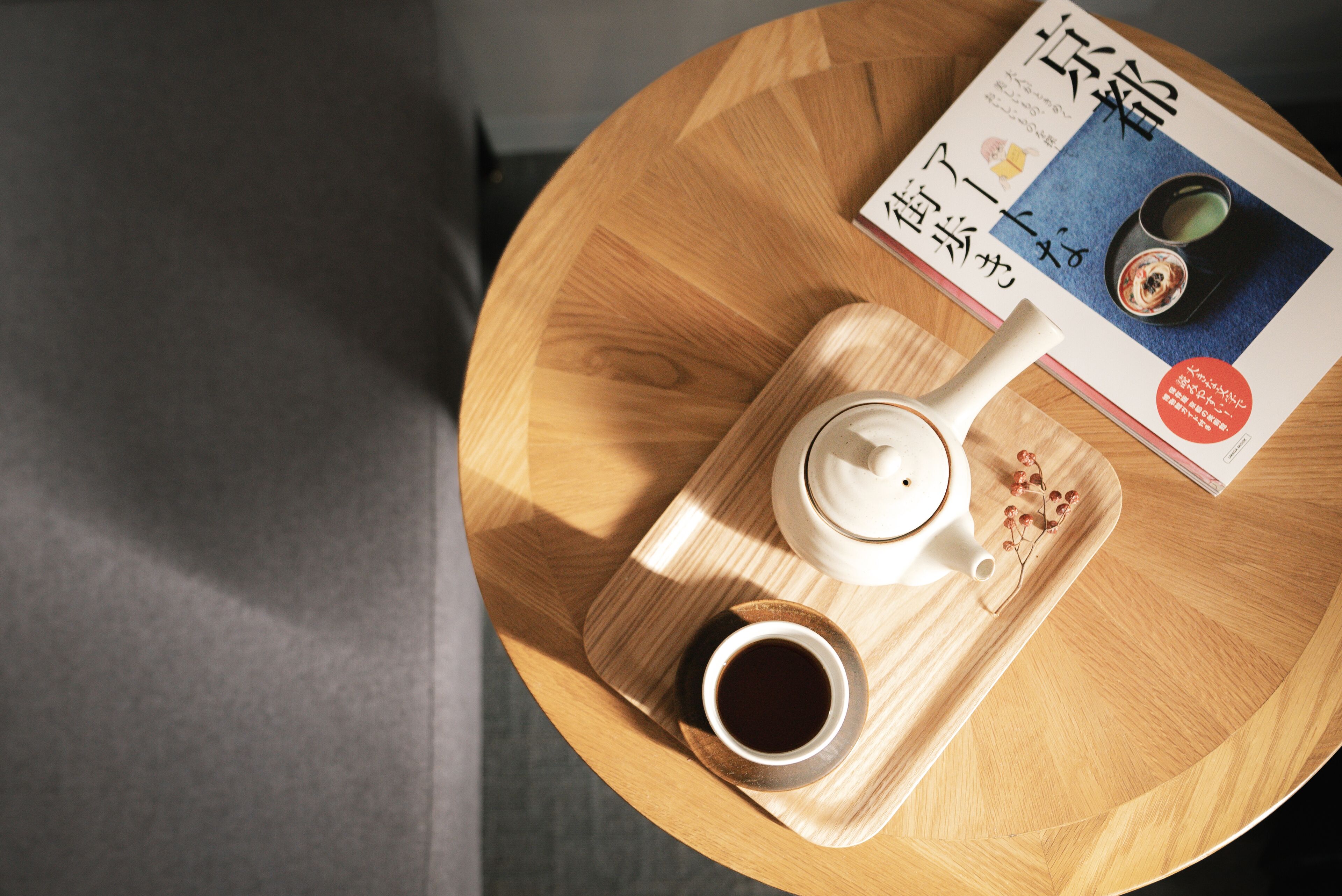 Una mesa redonda de madera con una tetera blanca, una taza de café y una revista.