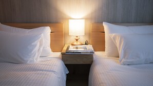 Ein Hotelzimmer mit zwei Betten, einem Nachttisch mit Lampe und einer Stapel Zeitschriften.