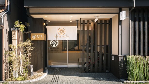 Ein Hotel Eingang mit einem traditionellen japanischen Tor, einem Schild und einem kleinen Garten.