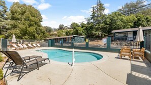 A swimming pool with lounge chairs and a small building, surrounded by a fence and trees.