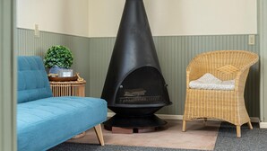 Une pièce avec un poêle à bois noir, un canapé bleu et un fauteuil en osier avec un coussin.