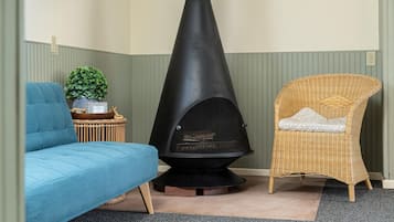 A room with a black wood-burning stove, a blue sofa, and a wicker chair with a cushion.