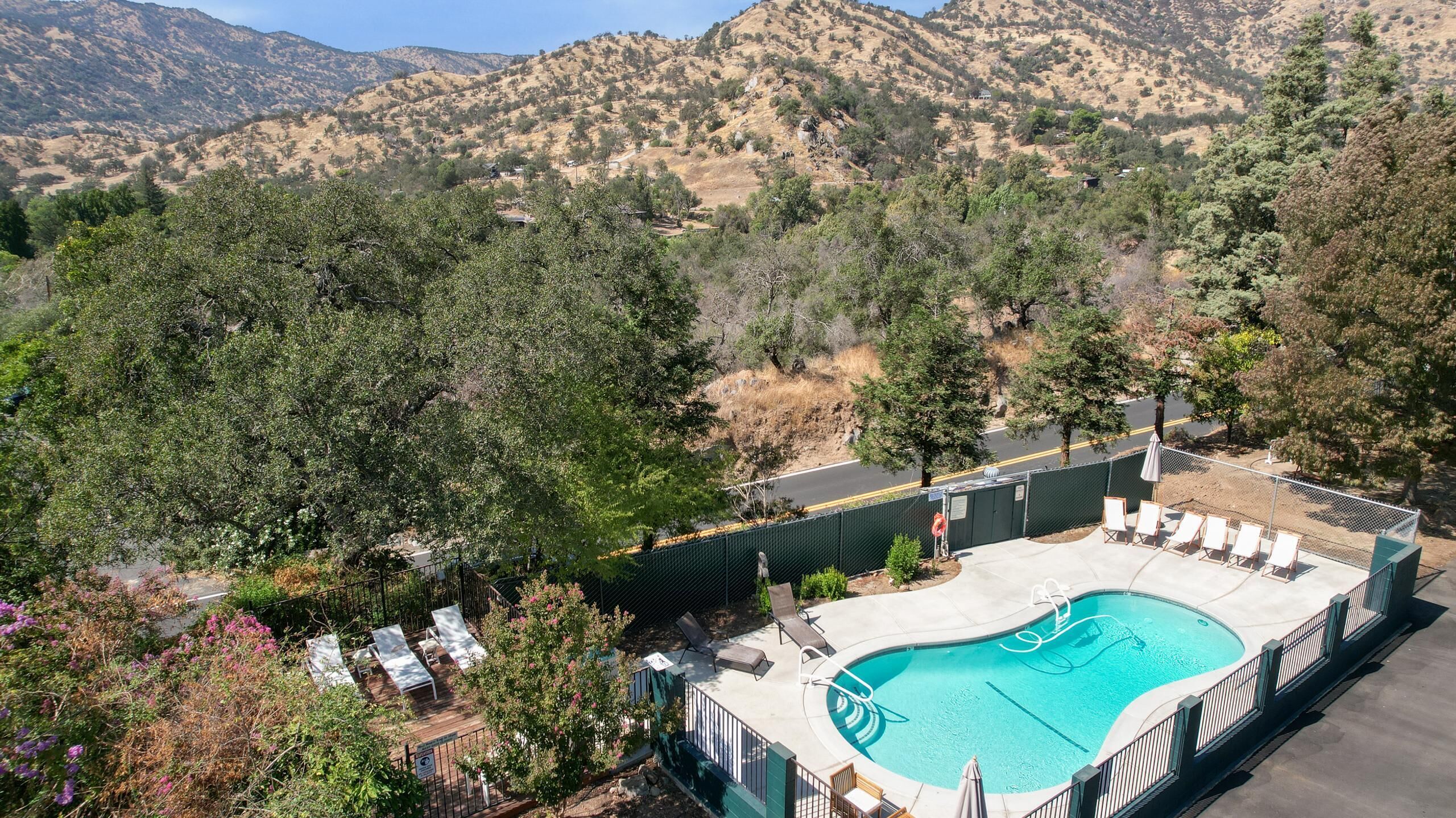 A pool area with lounge chairs, surrounded by trees and mountains in the background.