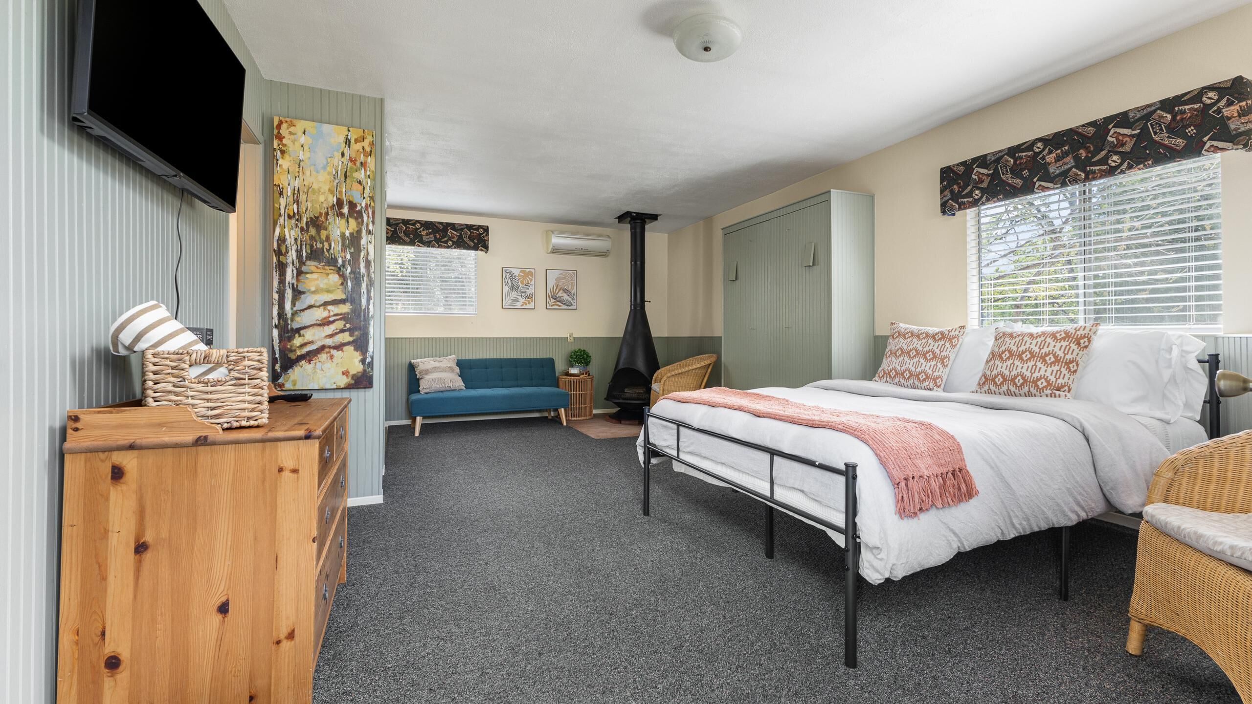 A bedroom with a bed, a sofa, a wooden dresser, a television, and artwork on the walls.