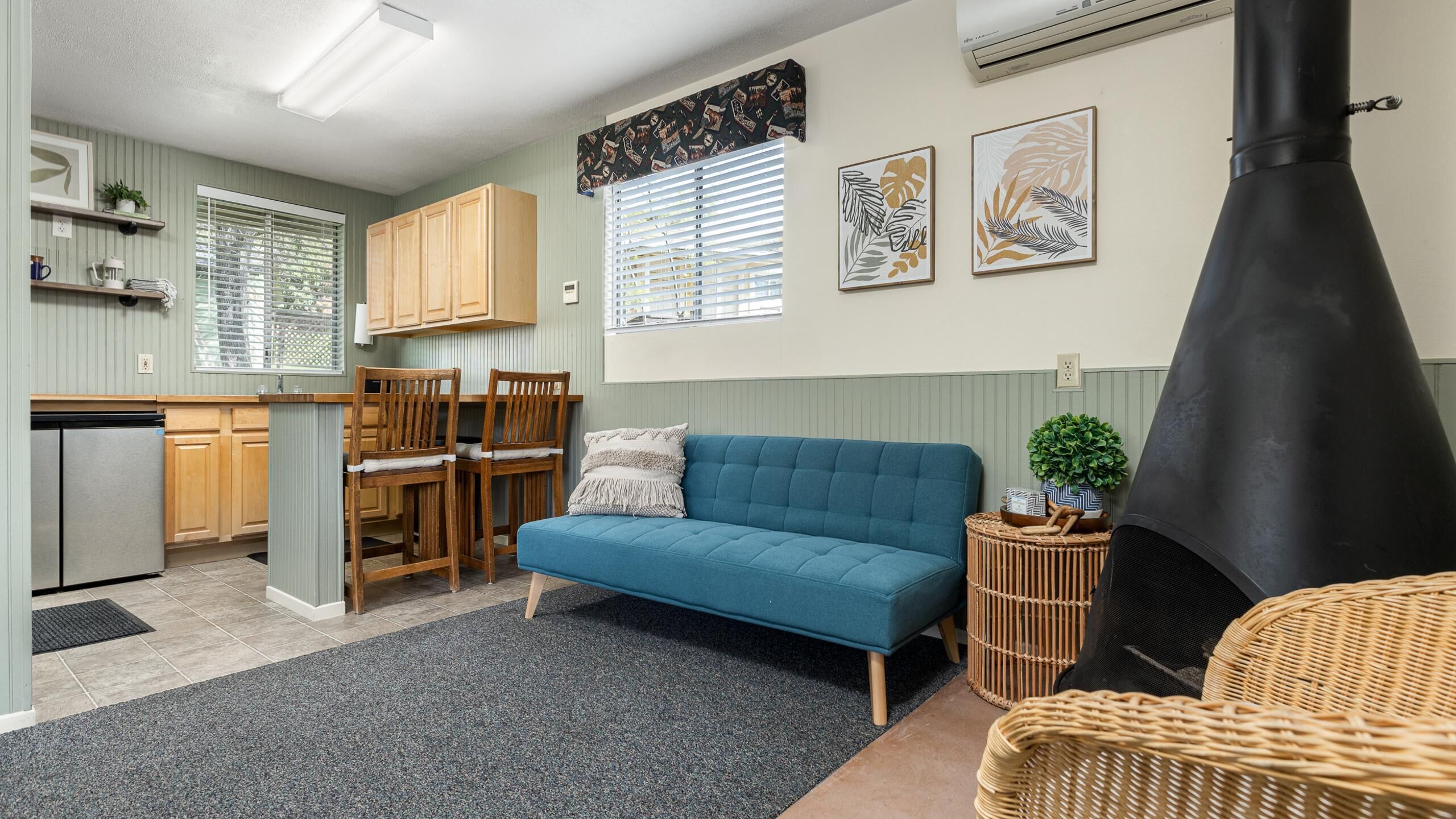 Ett kompakt bostadsutrymme med ett litet kök, en blå soffa, en matplats med trästolar och en svart spis.
