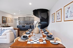 Uma área de refeições com toalha de mesa xadrez, pratos pretos e brancos, e um vaso central.