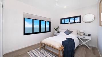 A modern bedroom with a large window, a ceiling fan, a bedside table with a lamp, and a bedside mirror.