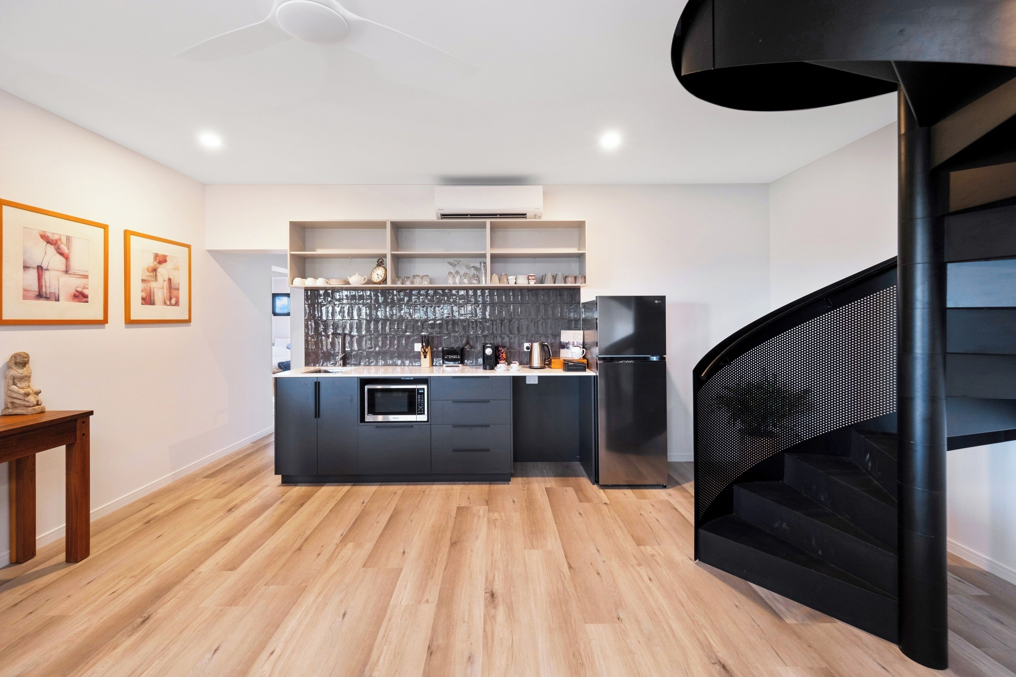 A modern kitchen with a central island, built-in shelves, and a black spiral staircase.