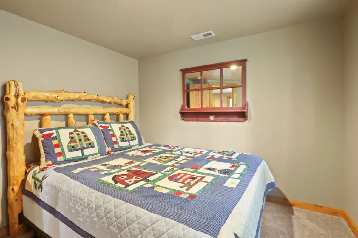 Een slaapkamer met een houten hoofdbord, een gewatteerde spreideken en een klein raam met spiegel.