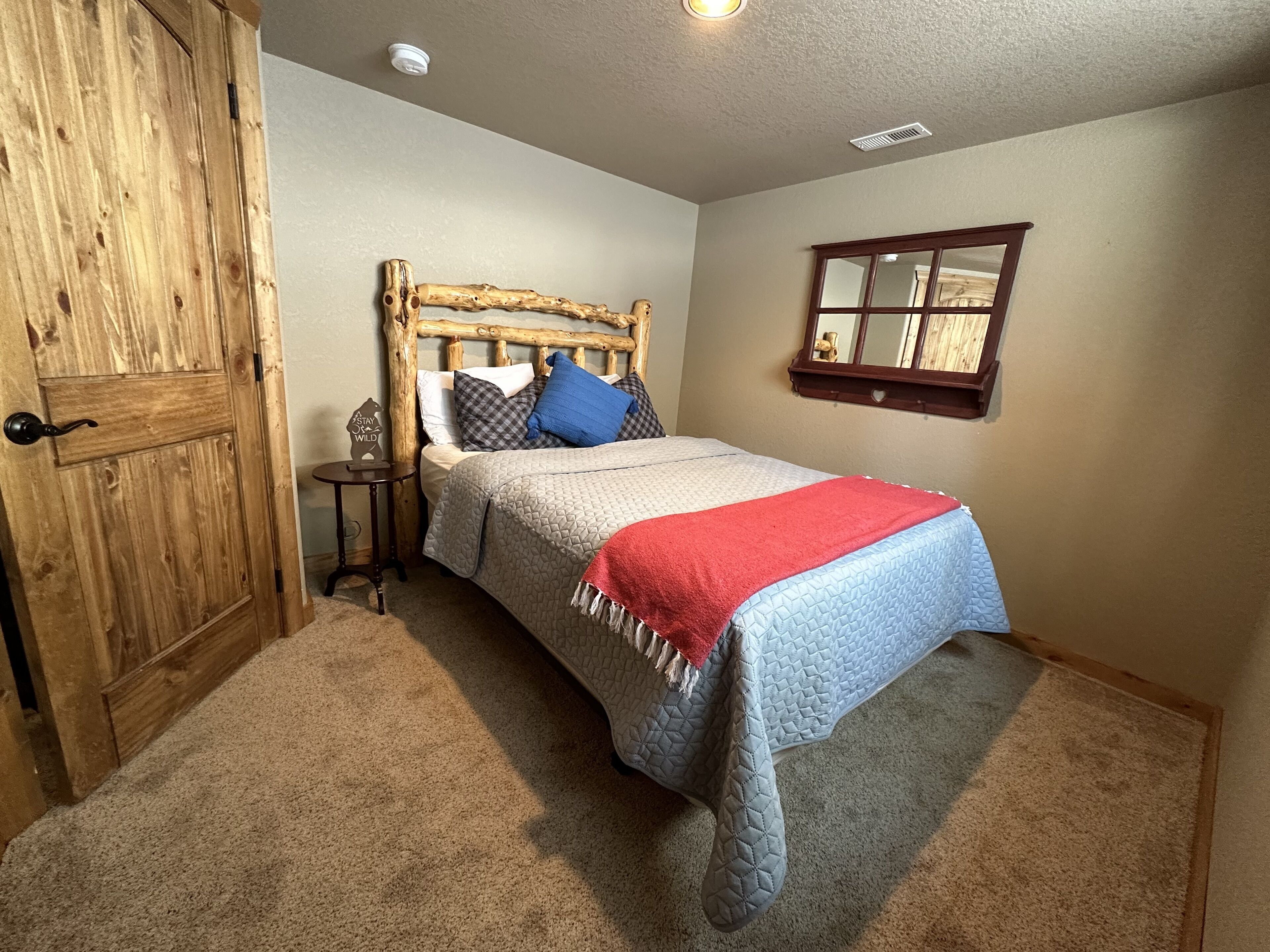 Une chambre avec une porte en bois, un lit recouvert d’une courtepointe matelassée, des oreillers, une petite table de chevet et un miroir au mur.