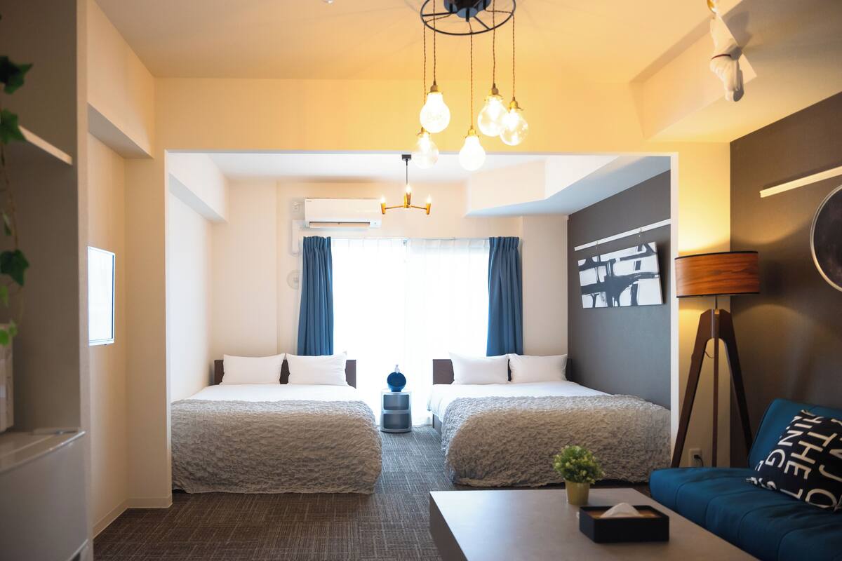 A hotel room with two beds, a sofa, a lamp, and a ceiling light fixture.