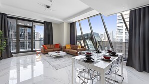 A modern living room with a dining area, large windows, and a city view.