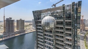 A modern high-rise building with a distinctive spherical glass structure, surrounded by construction cranes and other buildings.