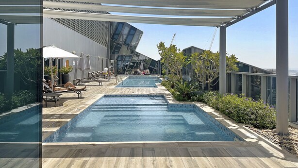 A rooftop pool area with multiple swimming pools, lounge chairs, and umbrellas.