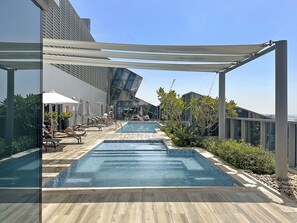 Ein Poolbereich auf dem Dach mit mehreren Schwimmbecken, Liegestühlen und Sonnenschirmen.