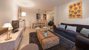 A modern living room with a dark sofa, a wooden coffee table, a TV, and a dining area with a table and chairs. - La Clusaz Primevères summer (La Clusaz)