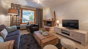 A cozy living room with a sofa, a wooden coffee table, a TV, and a fireplace. - La Clusaz Primevères summer (La Clusaz)