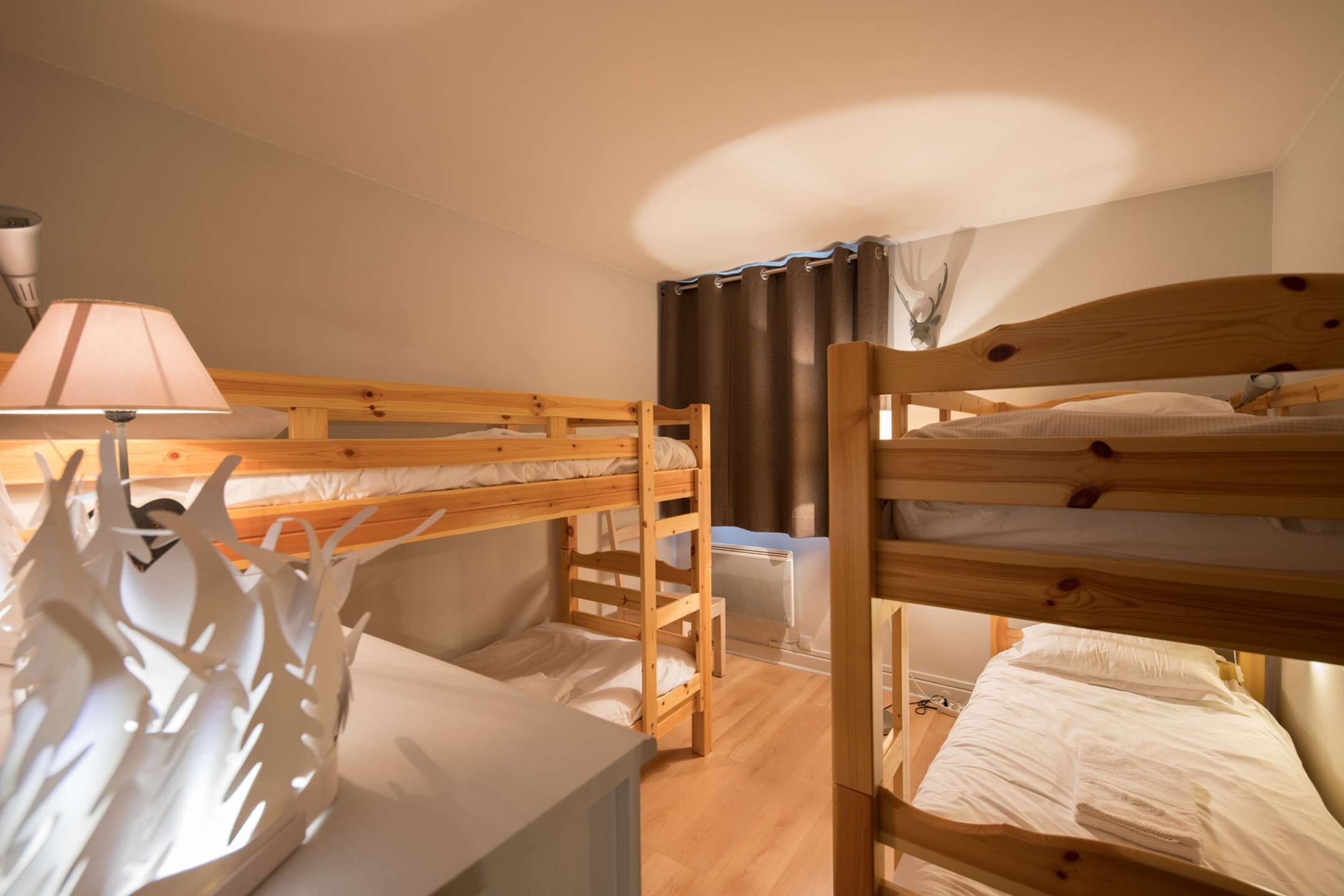 A bunk bed room with a wooden headboard, a bedside table with a lamp, and a window with curtains.