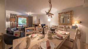 A dining area with a wooden table set for four, a chandelier, and a mirror with antlers. - La Clusaz Primevères summer (La Clusaz)